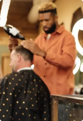A barber using a hairdryer to clean a customer's hair